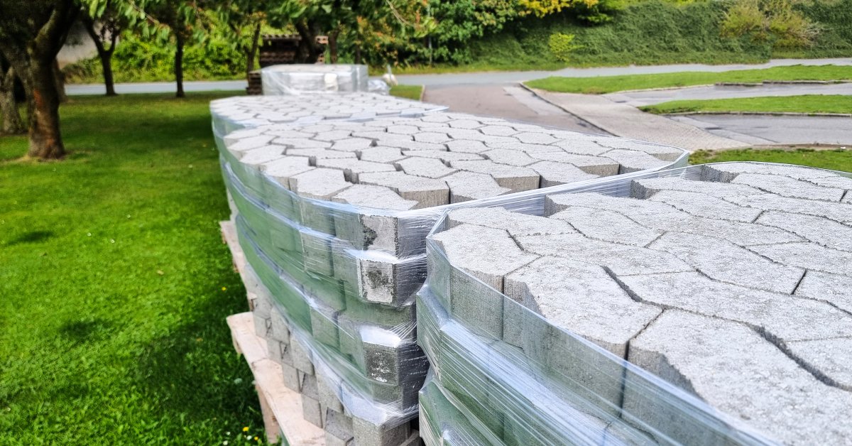 Close-up of a delivery of several pallets of grey interlocking paver stones stacked together at a project site.