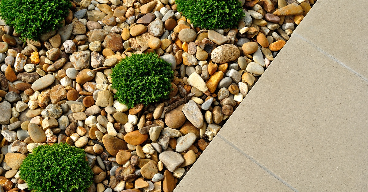 An aerial view of a sidewalk close up. The sidewalk is edged with landscape rock and mini green shrubs.