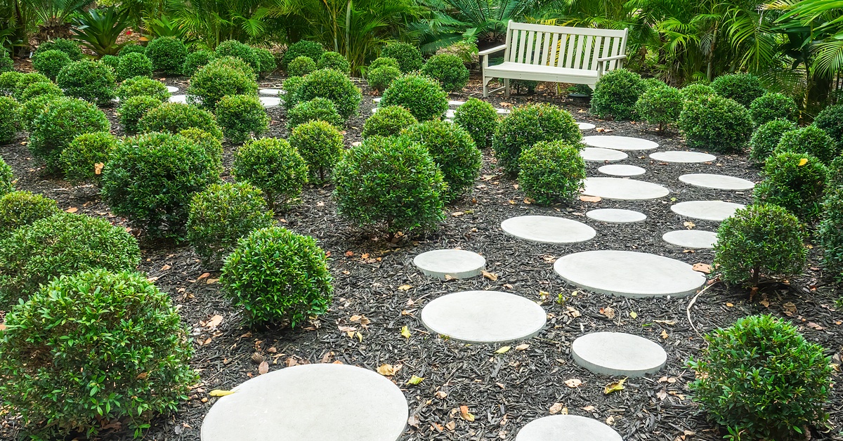 A backyard area with fresh landscaping, including round stepping stones and black mulch. There's a sitting bench in the back.