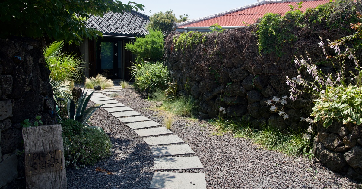 A gravel pathway leading up to a residential property with square stepping stones in the center of the gravel.