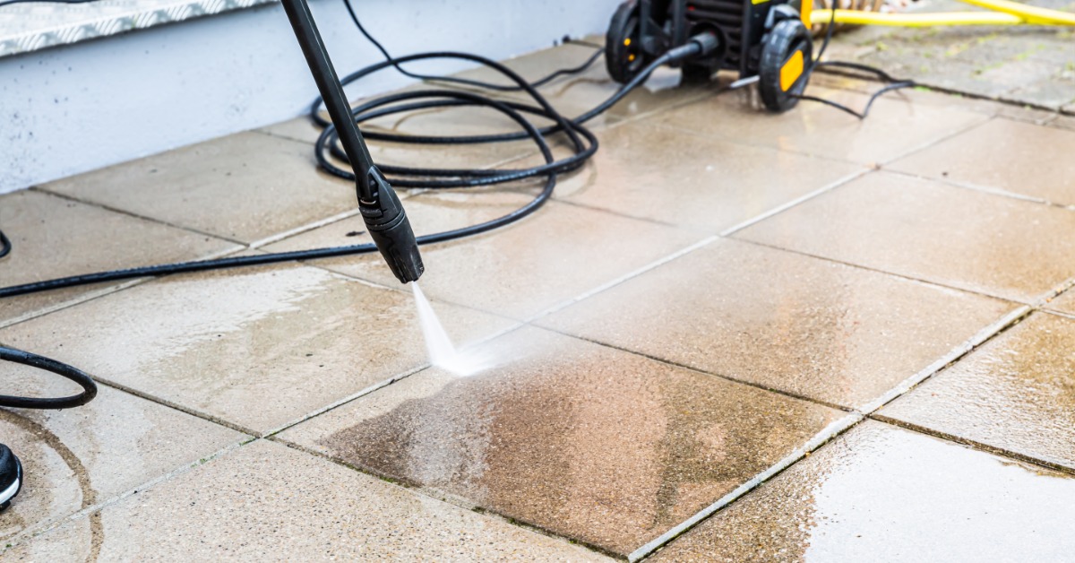 A close-up of a patio being washed with a pressure washer. The pavers are perfect squares and placed in neat rows.