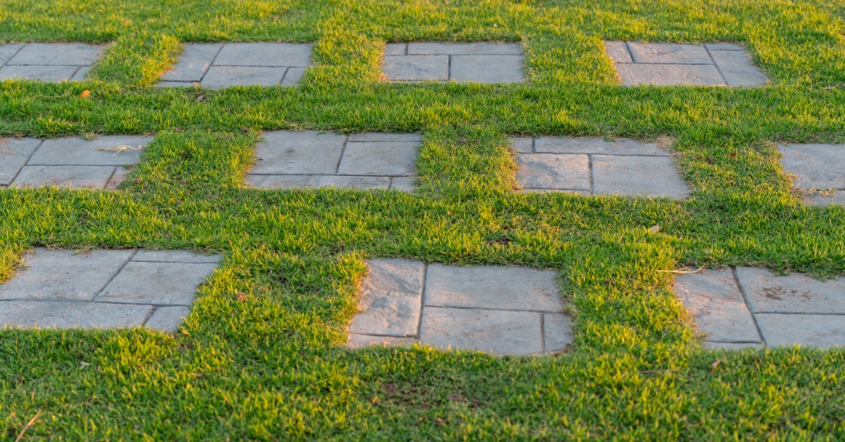 A backyard with perfectly spaced step stones sitting in the grass as a walkway. The stones are older, dark gray.