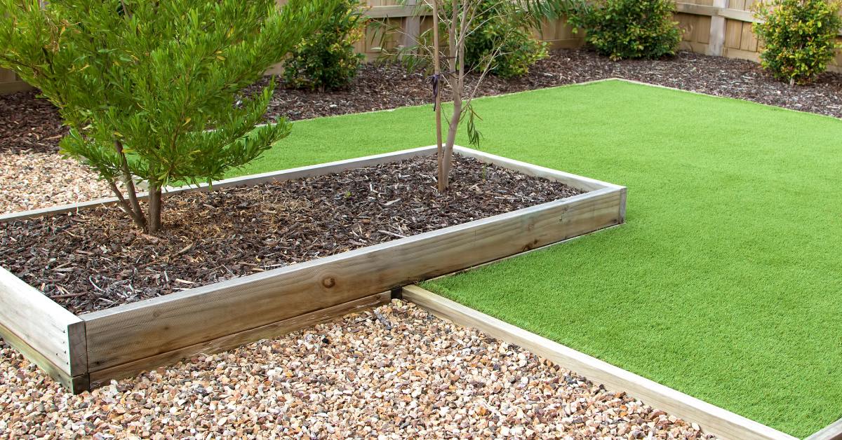 A backyard area with freshly mowed grass, a garden box with mulch, and landscape rock in a larger garden box.