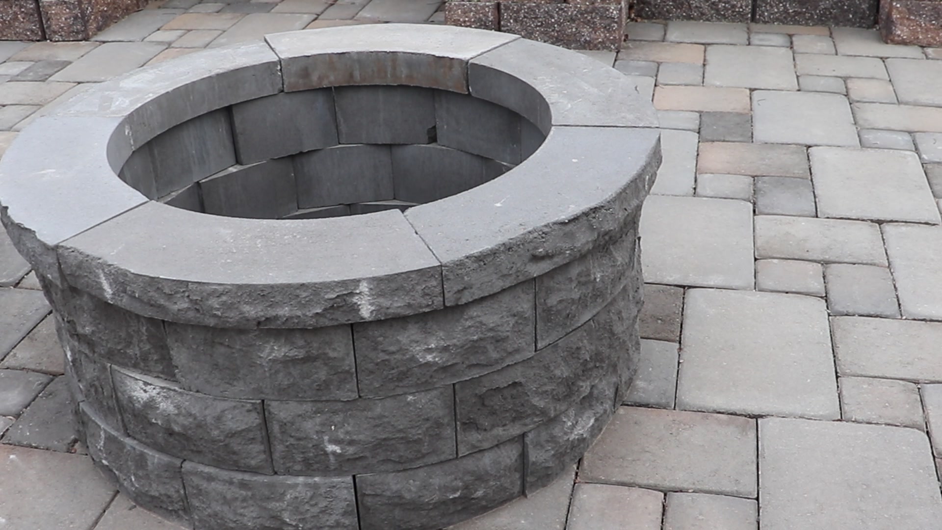A round fire pit kit built from concrete blocks on a paver patio